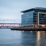Vancouver waterfront at dusk showing modern buildings, water reflections, and a distant stadium glow suggesting civic and sports news in 2026.